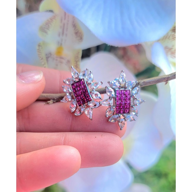 Precious - Art Deco 12.2 carat Ruby .925 Sterling Silver handmade earrings - Close-up of Art Deco ruby earrings on a hand with floral background.