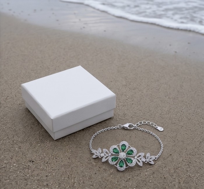 Giovanna - Authentic 7.9 carat Colombian Emerlad .925 Sterling Silver handcrafted Statement bracelet - Bracelet on sand with white box, featuring emerald and diamond floral design
