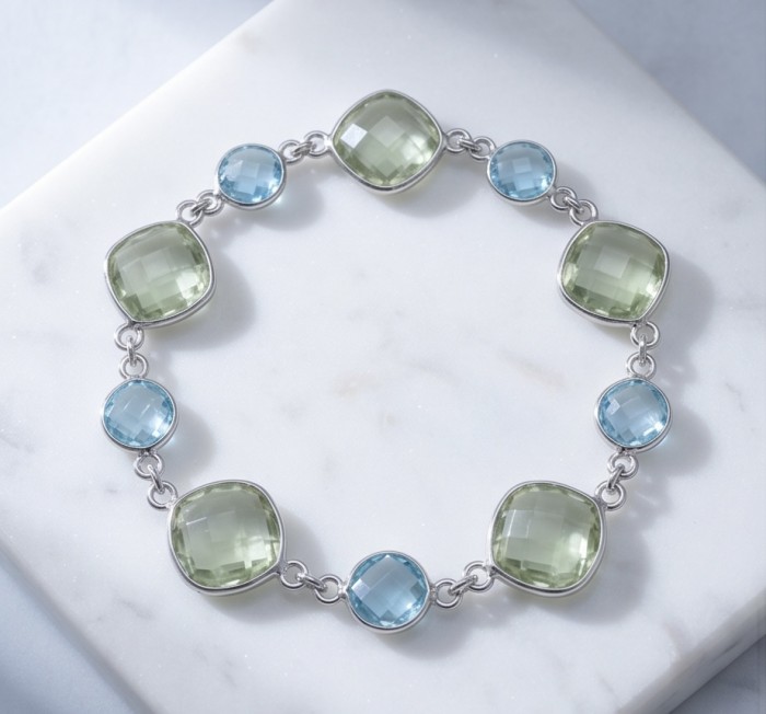 Authentic 22.5 carat Swiss Blue Topaz .925 Sterling Silver handmade Bracelet - Bracelet with blue topaz and green stones on marble background, top view.