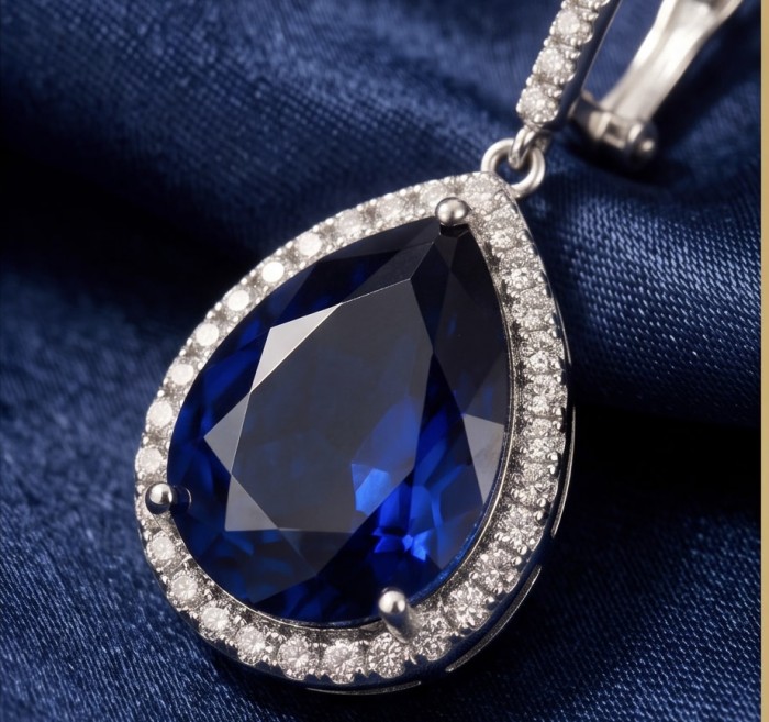 Vintage style - Marlyn - pear cut 14.9 carat Sapphire .925 Sterling Silver handcrafted earrings - Close-up of pear-cut sapphire pendant with diamond halo on fabric backdrop.