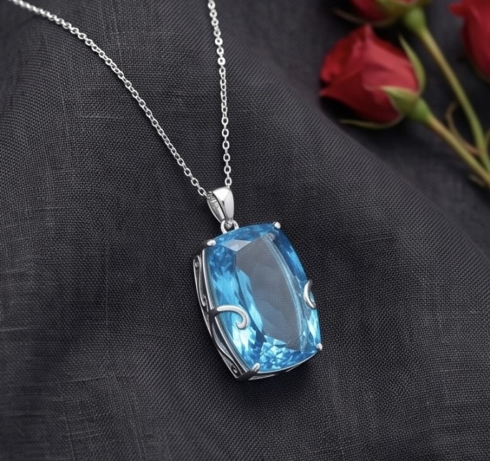 Tiffany Incredible baquette cut 32.4 carat Swiss Blue Topaz rhodium over .925 Sterling Silver handcrafted pendant - Front view of Tiffany Swiss Blue Topaz pendant on dark fabric background.