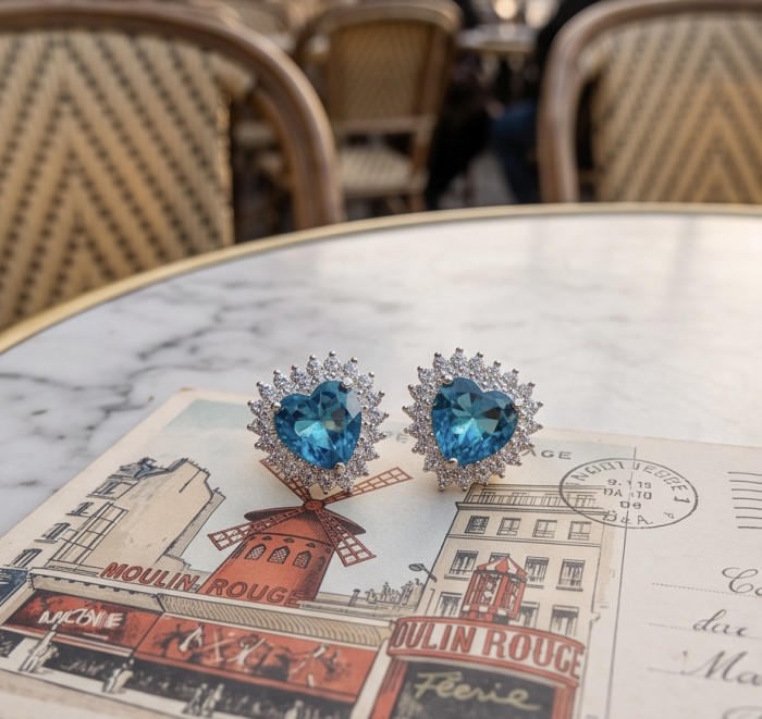 Heartes 6.7 carat Swiss Blue Topaz .925 Sterling Silver Handcrafted earrings - Swiss Blue Topaz earrings on table with Moulin Rouge postcard, close-up view.
