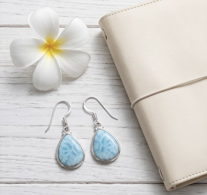 Caribbean Beauty Genuine 10.5 carat Blue Larimar .925 Sterling Silver handmade earrings - Blue Larimar earrings, top view, next to white flower and beige book.