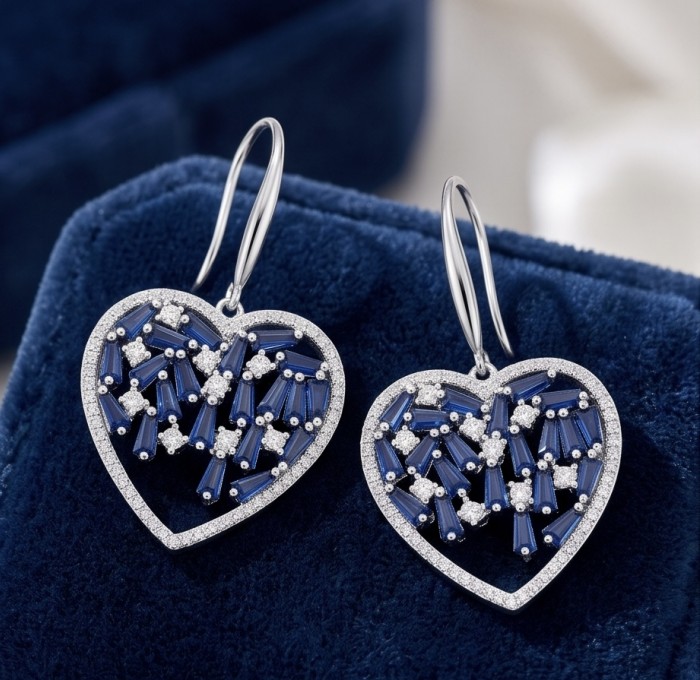 Precious Hearts - authentic 8.5 carat Sapphire .925 Sterling Silver dipped in rhodium handcrafted Statement Earrings - Heart-shaped sapphire earrings on blue fabric, front angle view.