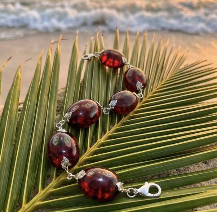 Excellent quality Cognac color Baltic Amber .925 Sterling Silver entirely handcrafted Bracelet - Baltic amber bracelet on palm leaf, beach background, side view.