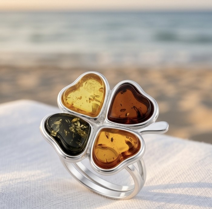 Golden Flower Authentic Baltic Amber rhodium over .925 Sterling Silver handcrafted ring; s. 7 adjustable - Beach background, close-up of heart-shaped amber clover ring on fabric.