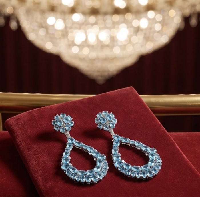 Atlantica 12.8 carat Swiss Blue Topaz 22K Gold over .925 Sterling Silver Handcrafted Statement earrings - Swiss Blue Topaz Earrings on red velvet with chandelier background