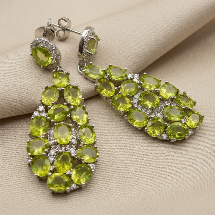Fiesta Authentic 27.5 carat Peridot .925 Sterling Silver brilliantly handcrafted Statement earrings - Peridot earrings on fabric, front view showing stones and settings.
