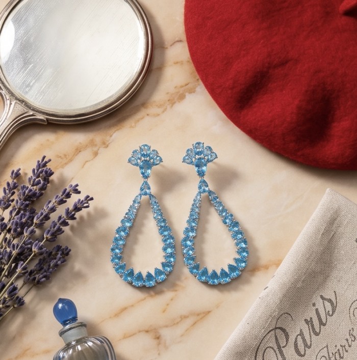 Atlantica - 12.5 carat Swiss Blue Topaz .925 Sterling Silver Handcrafted Statement Earrings - Topaz earrings on marble with red beret and mirror in flat lay.