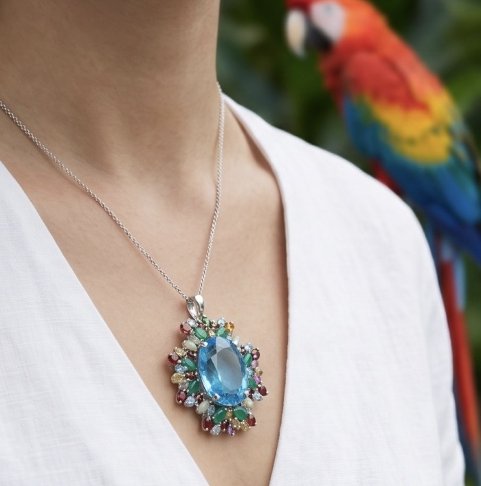 Oceania oval cut 47.8 carat Swiss Blue Topaz .925 Sterling Silver dipped in rhodium Handcrafted Pendant Brooch - Oceania Swiss Blue Topaz necklace worn on neck with parrot in background.