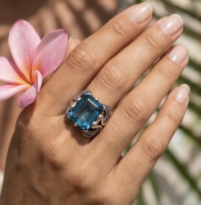 Two Swans Authentic 27.4 carat Aquamarine .925 Sterling Silver brilliantly handcrafted large Statement Ring size 8 - Aquamarine ring worn on hand, close-up with pink flower in background.