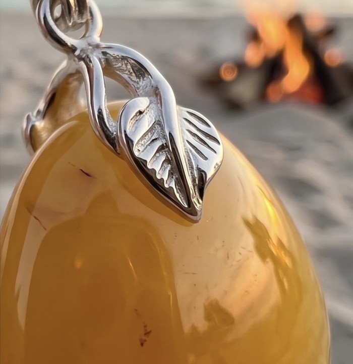 Prehistoric Authentic Golden Butterscotch Baltic Amber .925 Sterling Silver handcrafted Pendant - Close-up of amber pendant with silver leaf detail, beach fire in background.
