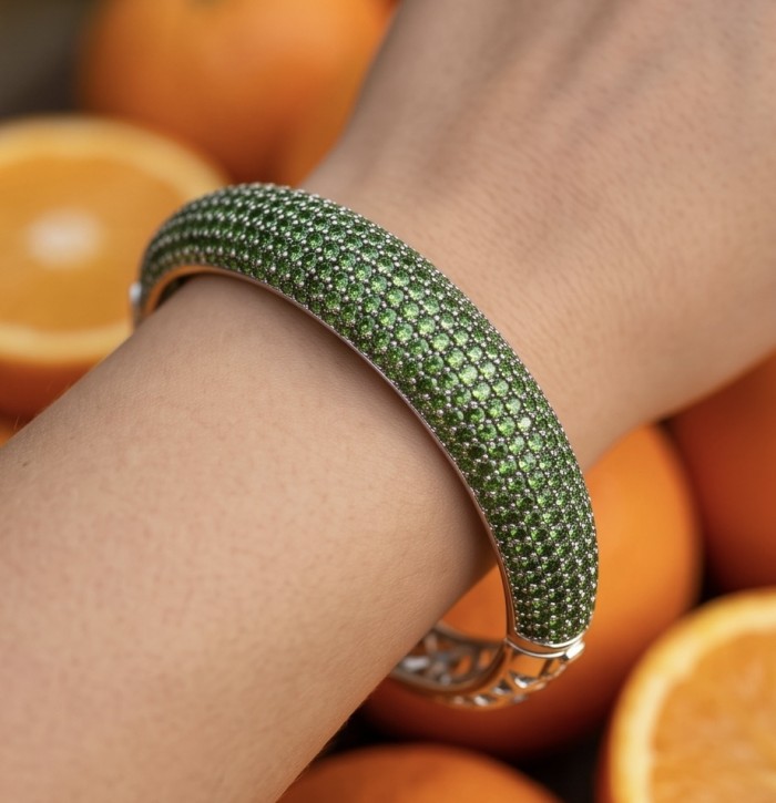 Authentic 10.9 carat pave Chrome Diopside .925 Sterling Silver dipped in Rhodium handcrafted Bracelet - Green pave bracelet detail worn on wrist, orange background.