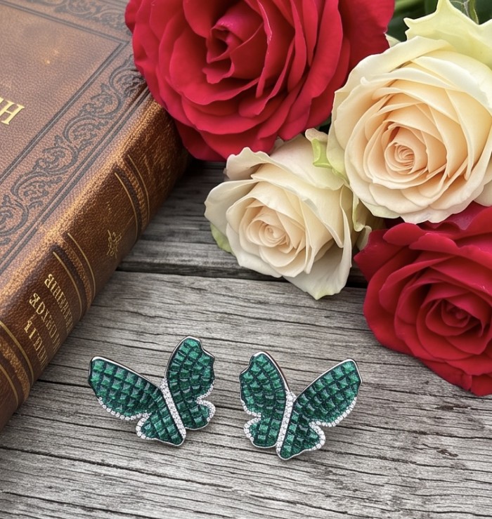 Incredible Butterflies genuine mystery setting 15.5 CARAT Emerald .925 Sterling Silver handcrafted Earrings - Butterfly earrings with emerald stones on wood near roses and book.