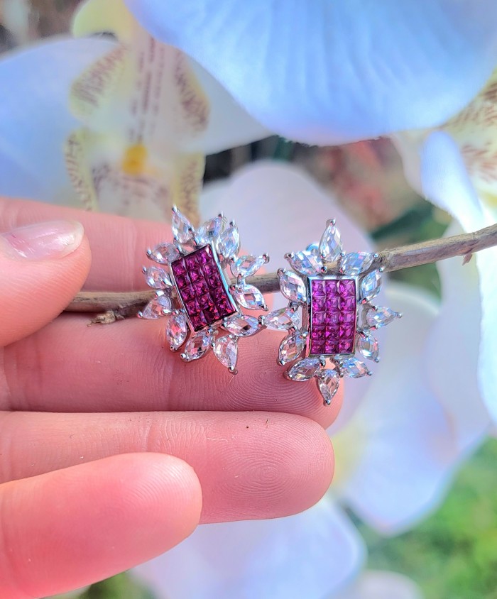 Precious - Art Deco 12.2 carat Ruby .925 Sterling Silver handmade earrings - Close-up of Art Deco ruby earrings on a hand with floral background.
